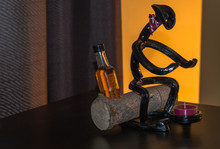 Horseshoe Cowboy Metal Art Sitting On A Log With A Bottle Of Whiskey Beside Him Warming Up Over A Candle Fire