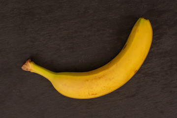 One whole ripe yellow banana flatlay on grey stone