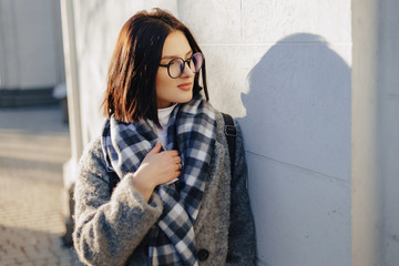 Wall Mural - Attractive young girl wearing glasses in a coat walking on a sunny day