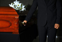 Young Man Carrying Wooden Casket In Funeral Home, Closeup