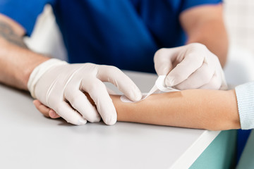 Wall Mural - medical patch. Doctor in blue uniform make elastic bandaged around a boy hand with trauma in his arm. in the hospital