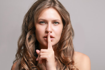 Beautiful young woman showing silence gesture on grey background