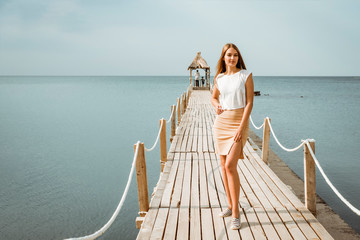 Wall Mural - Girl on the pier with a bungalow on the background of the sea.