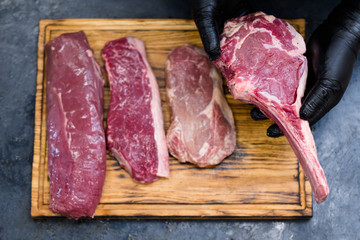 Steakhouse kitchen. Top view of raw beef meat assortment on wooden board. Chef cooking steaks.