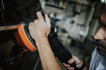 Car detailing - Hands with orbital polisher in auto repair shop. Selective focus.