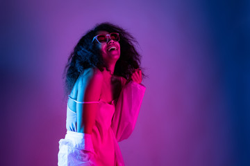 Happy beautiful fashion young african american girl hipster black woman wear stylish glasses eyewear and raincoat laughing dancing isolated on disco party purple pink trendy studio background