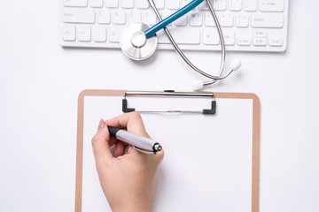 Wall Mural - Female doctor writing a medical record case over clipboard on white working table with stethoscope, computer keyboard. Top view, flat lay, copy space