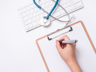 Wall Mural - Female doctor writing a medical record case over clipboard on white working table with stethoscope, computer keyboard. Top view, flat lay, copy space