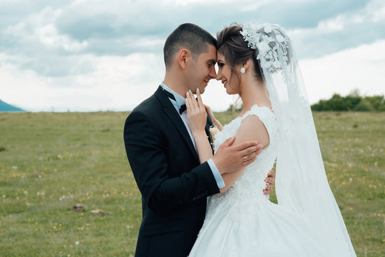 Beautiful bride and groom embracing and kissing on their wedding day outdoor. Newly married couple. Happy groom in black suit hugs her bride in a white dress. 