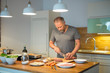 Mann schneidet Süsskartoffel mit dem Messer in der Küche und bereitet das Essen vor, Kartoffel, Fisch Filet, Möhren, grüner Salat, Knoblauch