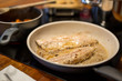 Fisch Filets braten in brauner Butter in Pfanne,  Topf mit Möhren im Hintergrund, Nahaufnahme