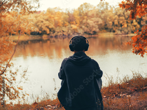 Fotomural The guy sitting on the Bank of the river and listens to music