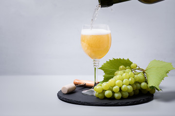 Wall Mural - Pouring white wine (champagne) from bottle into wineglass on gray background. Holiday celebration concept