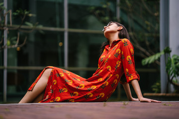 Portrait of a young, attractive Indian Asian woman in a traditional Indian orange dress smiling as she sits on a step in the city during the day.