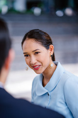 Wall Mural - Close up portrait of a beautiful, elegant, confident and attractive young Chinese Asian woman in a blue suit talking to a friend, a colleague or a recruiter during the day. She is smiling.