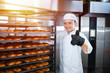 © salomonus_ - Baker with a hot baking trolley on a background of an industrial oven shows thumb up.
