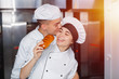 © salomonus_ - Boy baker kisses a girl on the cheek in a bakery against the background of the oven.