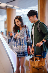 Wall Mural - A portrait of a pair of young and excited Asian travelers (Korean man and his Indian friend) checking in to board their plane for their holiday at an automated check-in booth in the airport.