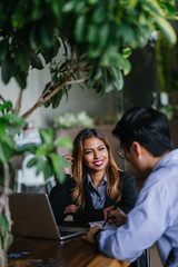 A young, tanned and attractive Southeast Asian woman in a suit is interviewing for a job to advance her career. She is smiling as she talks to her interviewer, a Chinese manager in a coworking office.