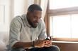 © fizkes - Young african american man using smartphone app sit on sofa