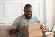 © fizkes - Smiling african man consumer open cardboard box get postal parcel