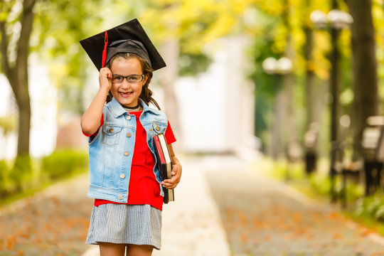 Authentic shot of cute little elegant girl with graduation hat is smiling during ceremony.