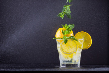 Wall Mural - Lemonade with flying mint and lemon. Summer refreshing drink with lemon on dark background. Infused water with citrus and mint. Levitation. Horizontal