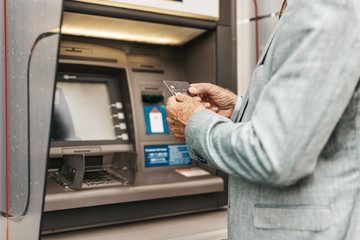 Wall Mural - Close up shot of senior man hand using bank credit card. He typing pin code on keypad of ATM machine.