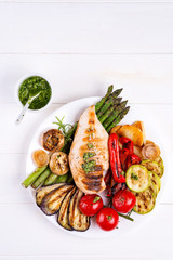 Wall Mural - Grilled chicken breast on a plate with grill vegetables on a wooden background, flat lay