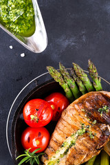 Wall Mural - Grilled chicken breast on a cast iron skillet with grill vegetables and green sauce on a stone background, flat lay