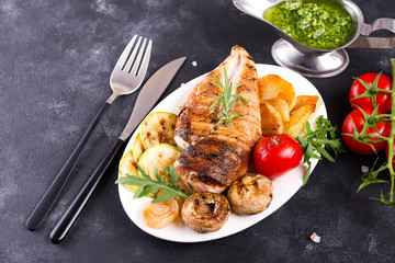 Wall Mural - Grilled chicken breast on a plate with tomatoes, mushrooms and green sauce on a stone background, flat lay