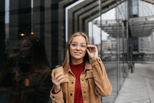 Portrait Of Young Beautiful Woman Wearing Stylish Eyeglasses, Walking Around Urban Street And Smiling. Hipster Girl With Happy Emotional Face Holding Cup Of Coffee Outdoor. Coffee Break Concept