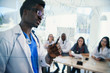 © gorynvd - African professor at medical conference in modern clinic teaches his students. Doctor writing on board some formulas for interns in conference room at hospital at sunrise.