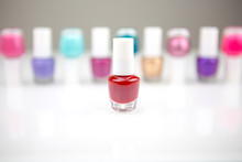 View On A Shiny White Desk Full Of Small Glass And Plastic Bottles With Assorted Nail Polish And Lacquer With Focus On One Red Nail Polish.