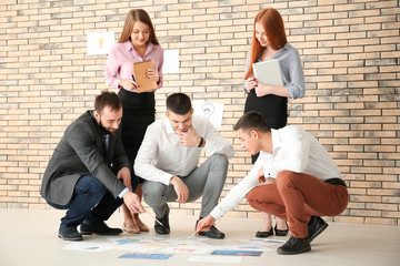 Poster - Young marketing expert and team working with papers on floor