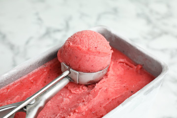 Container with delicious pink ice cream and scoop on marble table, closeup