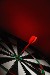 Color arrow hitting target on dart board against red background