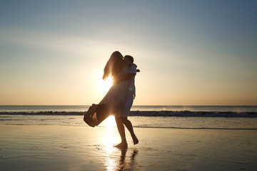 Young couple enjoying together on beach, young man spinning his girl in a circle. Couple dancing at sunset on the beach