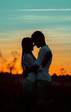 Silhouettes Of Happy Young People Hugging Each Other At Sunset In The Countryside In The Evening. Romantic Meeting Of Two Lovers Against The Background Of The Evening Sky.