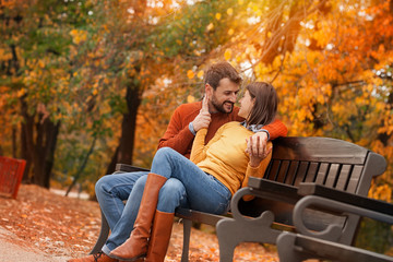 Young couple in love flirting on bench in autumn park