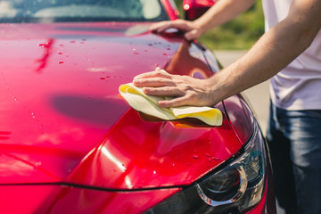 Car detailing - the man holds the microfiber in hand and polishes the car. Selective focus. Car detailing series : Worker cleaning red car. 