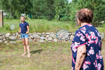 Aged grandmother trying to play badminton with her young granddaughter, outdoors