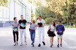 © Vitalii - Happy students going home after classes from the university with books and folders. Friends walking together in the park