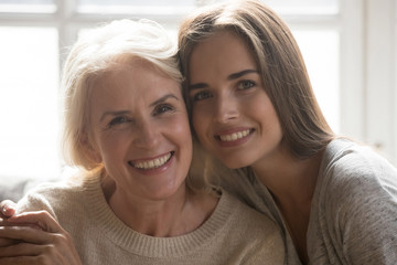 Wall Mural - Middle aged mother grown up daughter embracing looking at camera