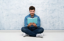 Young Man Sitting On The Floor Holding And Reading A Book