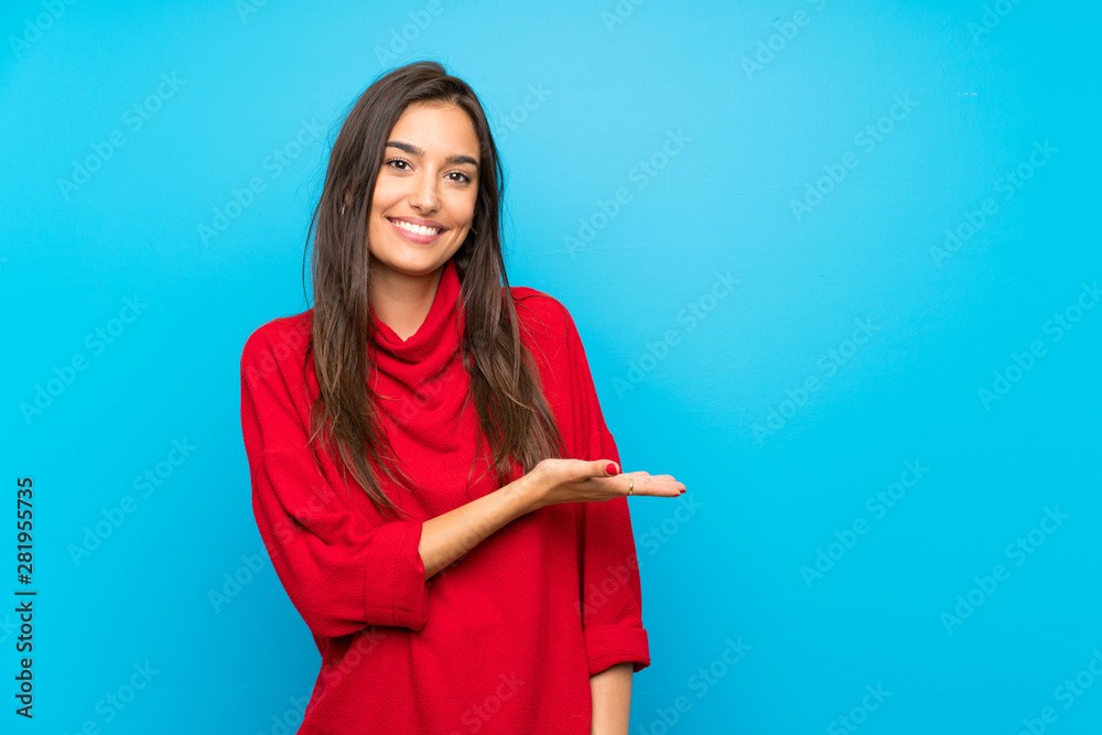 Young woman with red sweater over isolated blue background extending hands to the side for inviting to come - obrazy, fototapety, plakaty 