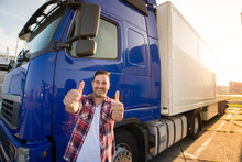 Portrait Of Happy Smiling Middle Aged Truck Driver Standing By His Truck And Holding Thumbs Up. Successful Transportation Service.
