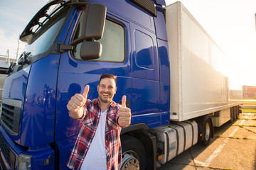 portrait of happy smiling middle aged truck driver standing by his truck and holding thumbs up. succ