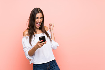 Wall Mural - Young woman over isolated pink background with phone in victory position
