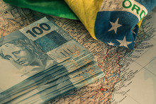 Brazilian Money, 100 Reais Banknotes On The Map Of Brazil With A Fragment Of The National Flag